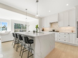 The kitchen features white cabinetry, a large center island with seating, a range with a tile backsplash, and light-toned flooring - 