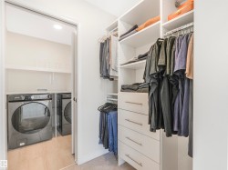 Walk-in closet featuring extensive built-in shelving, hanging rods, and drawers, with a laundry area visible through the doorway, equipped with a washer and dryer - 