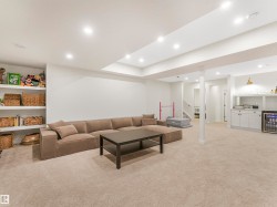 Spacious entertainment area featuring recessed lighting, built-in shelving, and a wet bar with shaker-style cabinetry and a beverage cooler - 