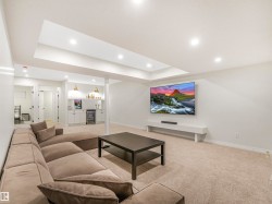 The room features recessed lighting, a built-in media console, and a wet bar with white cabinetry and shelving - 