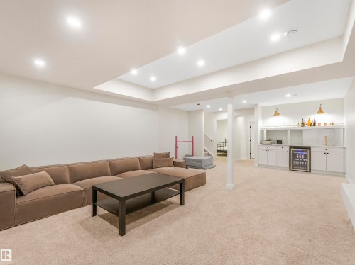 This expansive recreation room features recessed lighting, carpeted flooring, and a built-in wet bar with white cabinetry and a beverage cooler - 19 Nettle Crescent, St. Albert, AB - Indoor