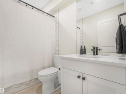 The bathroom features a toilet, a vanity with a white countertop and dark knobs, and white subway tile accents on the wall - 