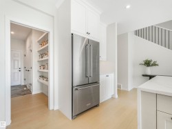 The kitchen features a stainless steel refrigerator, white cabinetry, and light-colored flooring - 