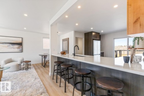 Modern kitchen featuring a white countertop island with seating, dark wood-finish cabinetry, and recessed lighting - 4508 109A Avenue, Edmonton, AB - Indoor