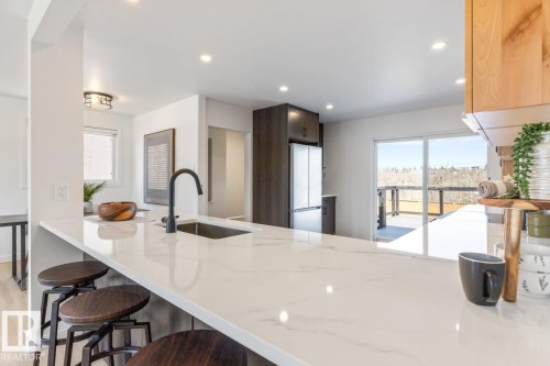 Kitchen island with a white stone-finish countertop and undermount sink with a matte black faucet - 4508 109A Avenue, Edmonton, AB - Indoor Photo Showing Kitchen With Upgraded Kitchen