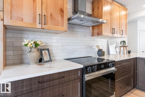 Kitchen featuring a stainless steel range hood, light wood upper cabinetry, dark wood lower cabinetry, white subway tile backsplash, and a white countertop with subtle veining - 4508 109A Avenue, Edmonton, AB - Indoor Photo Showing Kitchen