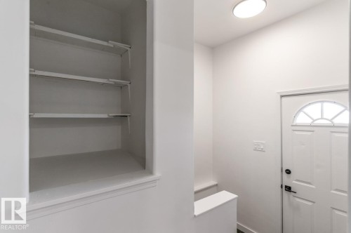 Recessed shelving unit featuring multiple adjustable shelves, a domed entry door with decorative glass, and a flush-mount ceiling light fixture - 4508 109A Avenue, Edmonton, AB - Indoor