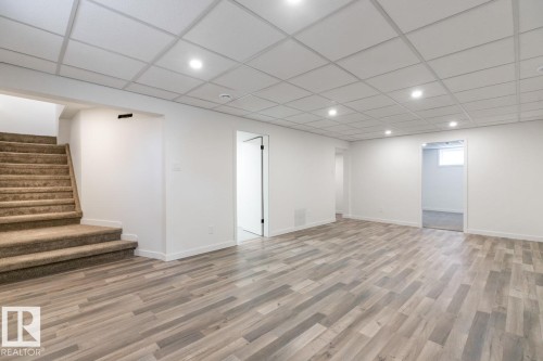 Spacious finished basement featuring wood-finish flooring, recessed lighting, white walls, drop ceiling, and carpeted stairs - 4508 109A Avenue, Edmonton, AB - Indoor