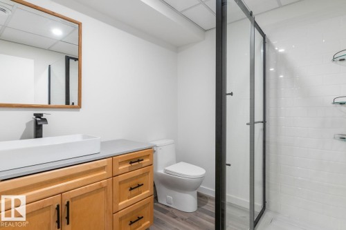 Bathroom featuring a light wood-finish vanity with a rectangular vessel sink, matte black faucet, and a large mirror with a wood frame - 4508 109A Avenue, Edmonton, AB - Indoor Photo Showing Bathroom