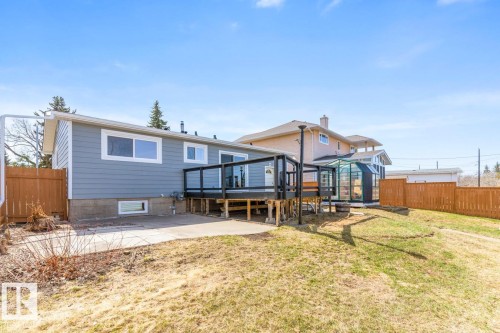 Rear exterior featuring a raised deck with dark railings, a concrete patio, and a sloped lawn - 4508 109A Avenue, Edmonton, AB - Outdoor With Deck Patio Veranda