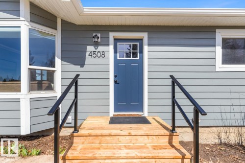 Entryway featuring light grey horizontal siding, a deep blue front door with window panes, and a modern exterior light fixture - 4508 109A Avenue, Edmonton, AB - Outdoor With Exterior