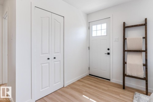 Entryway featuring wood-finish flooring, a white paneled door with glass inserts, and a bifold closet with black hardware - 4508 109A Avenue, Edmonton, AB - Indoor