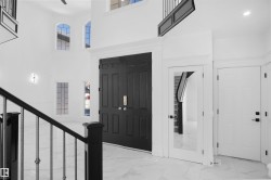 Two-story entryway featuring a double black paneled door, high ceilings, arched windows, a contemporary wall sconce, and marble-finish flooring - 