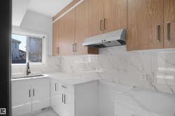 Kitchen featuring white shaker-style base cabinetry, wood-finish upper cabinetry, white stone-finish countertops, and a white tile backsplash - 