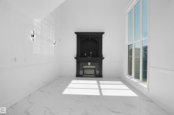 Spacious room featuring a grand black fireplace with an ornate mantel, towering multi-pane windows, white marble-look tile flooring, and elegant wall sconces - 