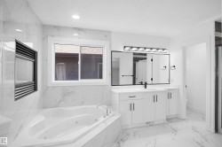 Spacious bathroom featuring a corner jetted soaking tub, a built-in electric fireplace, and a double vanity with matte black hardware - 