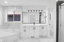 Contemporary bathroom featuring a corner soaking tub with deck-mounted fixtures, a large vanity with white cabinetry and dark hardware, a spacious counter with an integrated sink, a rectangular mirror, and a modern light fixture - 