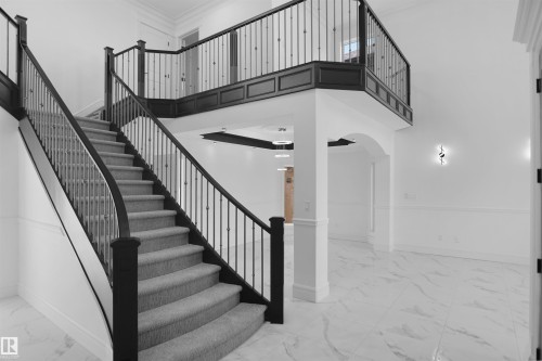 Curved staircase featuring dark wood newel posts and railings with decorative metal balusters, complemented by a carpeted tread - 6823 18 Avenue, Edmonton, AB - Indoor Photo Showing Other Room