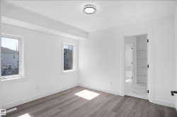 Bright room featuring wood-finish flooring, white painted walls, two windows with white trim, a decorative flush-mount ceiling light, and an open doorway revealing built-in shelving - 