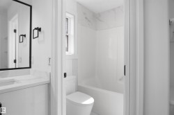 Contemporary bathroom featuring a vanity with an integrated sink and white countertop, black-framed mirror, and a toilet with a window above - 