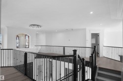 Spacious upper-level landing featuring dark wood-finish flooring, black wrought iron railings, recessed lighting, and a contemporary multi-tiered chandelier - 
