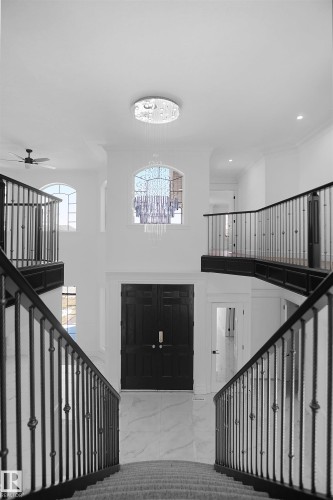Grand foyer featuring a two-story ceiling, a contemporary chandelier, dual curved staircases with wrought iron balusters, and a dark wood-paneled double entry door - 6823 18 Avenue, Edmonton, AB - Indoor Photo Showing Other Room