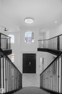 Grand foyer featuring a two-story ceiling, a contemporary chandelier, dual curved staircases with wrought iron balusters, and a dark wood-paneled double entry door - 