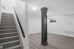 Carpeted staircase with a black handrail leading to a finished lower level featuring wood-finish flooring, a decorative column, recessed lighting, and built-in cabinetry - 