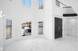 Two-story foyer featuring large grid-pattern windows, a black paneled double-door entry, and white marble-look flooring - 