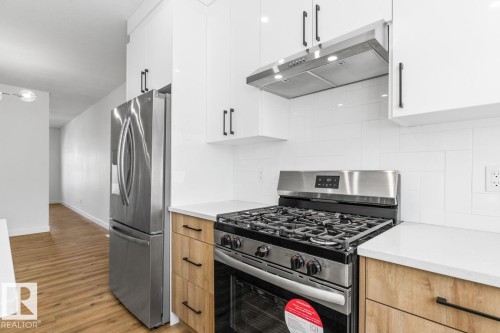 Modern kitchen featuring stainless steel appliances, white subway tile backsplash, white upper cabinetry with matte black hardware, wood-finish lower cabinetry, and light countertops - 6625 46 Avenue, Beaumont, AB - Indoor Photo Showing Kitchen