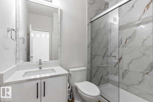 Bathroom featuring a spacious walk-in shower with floor-to-ceiling tile, a single vanity with a white countertop and integrated sink, a rectangular mirror, and chrome fixtures - 6625 46 Avenue, Beaumont, AB - Indoor Photo Showing Bathroom