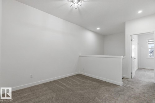 Carpeted landing area featuring a white half-wall railing, recessed ceiling lighting, and a chrome-finish flush mount ceiling fixture - 6625 46 Avenue, Beaumont, AB - Indoor Photo Showing Other Room