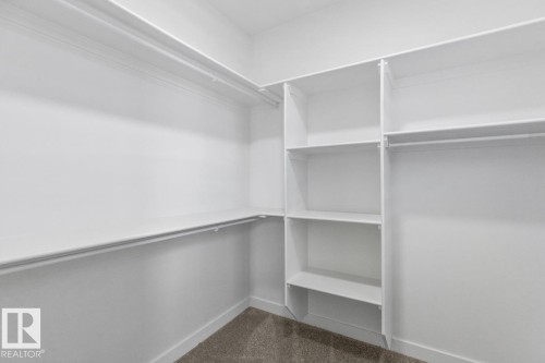 Walk-in closet featuring white built-in shelving, multiple hanging rods, and neutral carpet flooring - 6625 46 Avenue, Beaumont, AB - Indoor With Storage