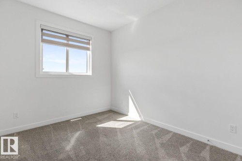 Bright room featuring a large window with horizontal blinds, plush grey carpet, white walls, and white baseboards - 6625 46 Avenue, Beaumont, AB - Indoor Photo Showing Other Room