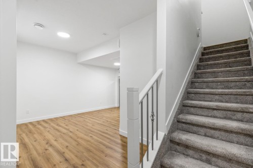Carpeted staircase with contemporary metal balusters and a white newel post, complementing the wood-finish flooring in the adjacent room - 6625 46 Avenue, Beaumont, AB - Indoor Photo Showing Other Room
