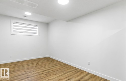 Room featuring wood-finish flooring, white baseboards, and bright white walls - 6625 46 Avenue, Beaumont, AB - Indoor Photo Showing Other Room