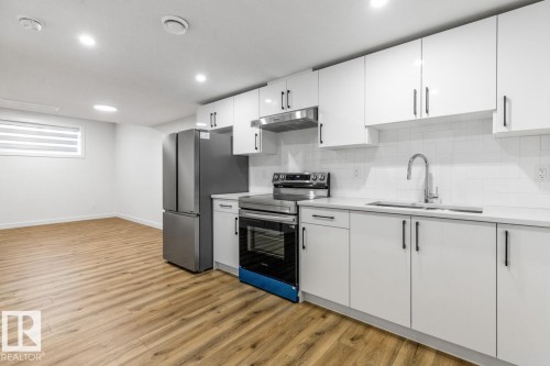 Kitchen featuring white cabinetry, stainless steel appliances, a stainless steel sink with a chrome faucet, light-toned countertops, and wood-finish flooring - 6625 46 Avenue, Beaumont, AB - Indoor Photo Showing Kitchen