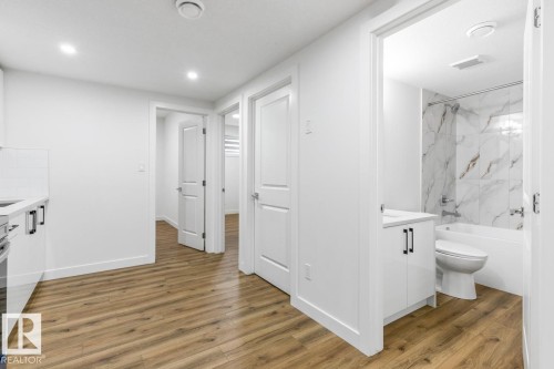 Bathroom featuring a white vanity with black hardware, a white bathtub with a shower, and a white and brown veined tile surround - 6625 46 Avenue, Beaumont, AB - Indoor Photo Showing Bathroom