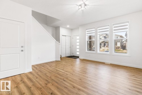 Spacious living area featuring wood-finish flooring, white walls, and a contemporary ceiling light fixture - 6625 46 Avenue, Beaumont, AB - Indoor Photo Showing Other Room
