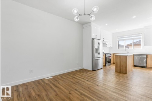 Open-concept kitchen and dining area featuring wood-finish flooring, a contemporary chandelier, stainless steel appliances, and a central island with a light-toned countertop - 6625 46 Avenue, Beaumont, AB - Indoor Photo Showing Kitchen