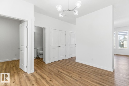 Open interior space featuring wood-finish flooring and a contemporary overhead light fixture - 6625 46 Avenue, Beaumont, AB - Indoor Photo Showing Other Room