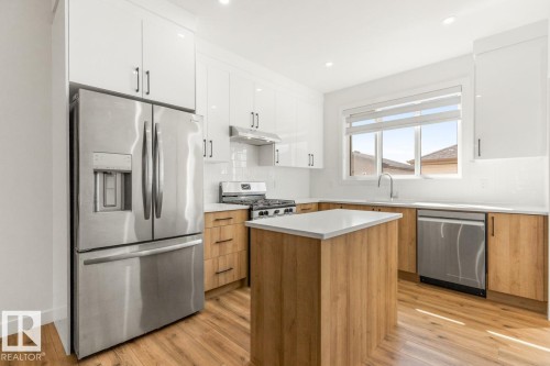 Contemporary kitchen featuring a central island with a light wood-finish base, white countertop, and integrated stainless steel appliances - 6625 46 Avenue, Beaumont, AB - Indoor Photo Showing Kitchen