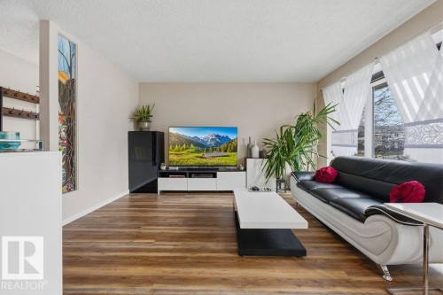 Spacious living area featuring wood-finish flooring, neutral wall tones, and a decorative stained glass panel - 7422 188 Street, Edmonton, AB - Indoor