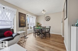 Open-concept living and dining area featuring wood-finish flooring, neutral wall paint, and multiple windows - 