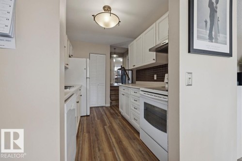 Galley kitchen featuring white cabinetry, wood-finish flooring, white appliances, and a dark tiled backsplash - 7422 188 Street, Edmonton, AB - Indoor Photo Showing Kitchen