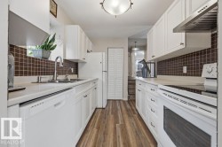 Galley kitchen featuring white cabinetry, wood-finish flooring, a mosaic tile backsplash, and a double basin stainless steel sink - 