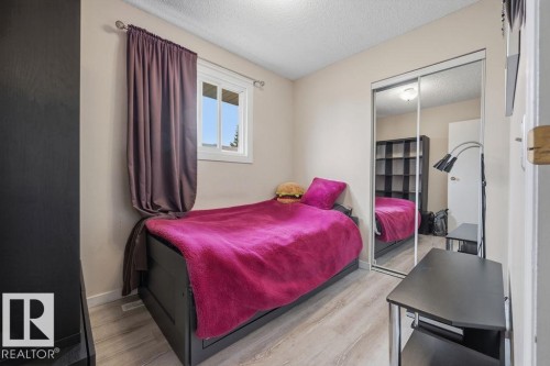 Bedroom featuring a window with a white frame, wood-finish flooring, and a mirrored sliding closet door - 7422 188 Street, Edmonton, AB - Indoor Photo Showing Bedroom