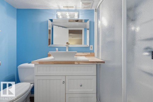 Bathroom featuring a white shaker-style vanity with wood-finish countertop, a rectangular vessel sink with a chrome faucet, and a frameless mirror with an overhead light fixture - 7422 188 Street, Edmonton, AB - Indoor Photo Showing Bathroom