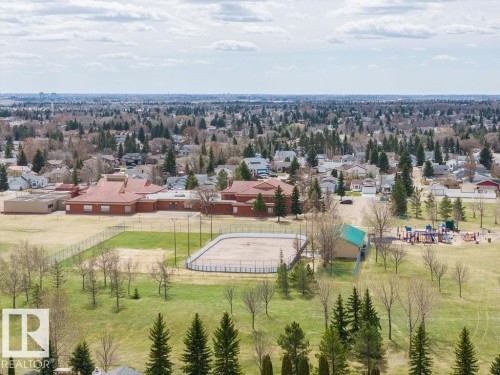 Expansive green space featuring an outdoor rink, a playground, and mature trees, surrounded by residential properties and a brick building with a red roof - 7422 188 Street, Edmonton, AB - Outdoor With View