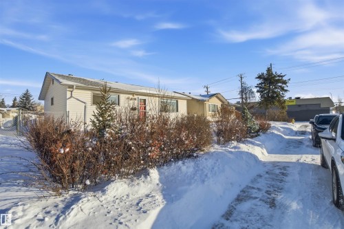 The property features a light-colored exterior and a red front door, set against a backdrop of snow-covered shrubs and evergreens - 5208 90 Avenue, Edmonton, AB - Outdoor